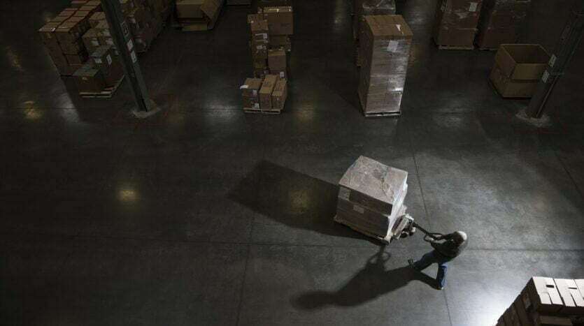 Warehouse worker using a manual pallet jack to move some products in a distribution warehouse.