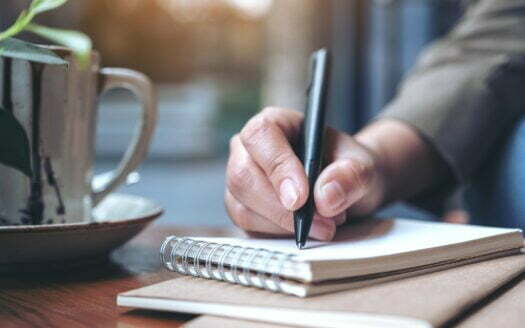 Closeup image of a woman's hand writing on blank notebook with coffee cup on wooden table