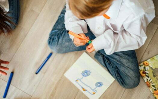 The boy draws a car with felt-tip pens, sitting on the floor at home